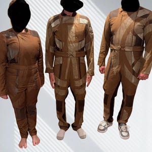 May include: Three brown jumpsuits featuring a patchwork design with varying shades of tan and dark brown fabric. Each garment includes a structured collar, long sleeves, a fitted waist belt, and reinforced paneling on the shoulders and legs.