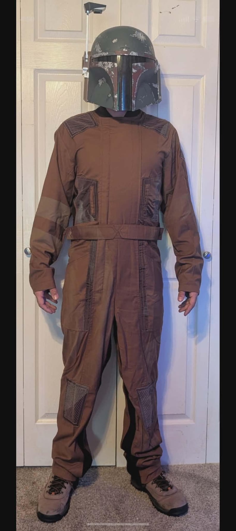 May include: A full-body brown jumpsuit featuring dark brown textured panels on the shoulders, waist, and knees, paired with a weathered green and dark gray helmet with a black visor and a side-mounted antenna, worn with brown lace-up boots.