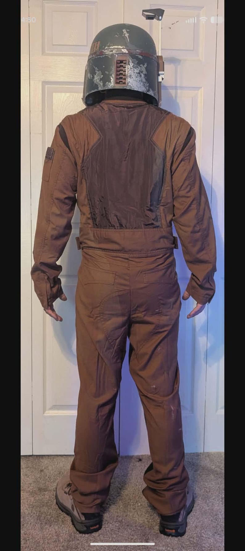 May include: A brown jumpsuit with a dark brown back panel and long sleeves, paired with a weathered green and silver helmet featuring a T-shaped visor and a side-mounted antenna. The outfit is worn with grey and black hiking boots.