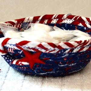 May include: A fabric bowl with a patriotic design, featuring red, white, and blue colors. The bowl is filled with white items and has a red star applique on the side. A separate red star is also visible.