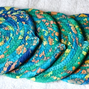 May include: Set of four round coasters with a spiral design. The coasters are made of fabric in shades of blue, green, yellow, and orange. The coasters are approximately 4 inches in diameter.