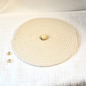 May include: A white rope circle with a white ball in the center. There are two smaller white balls on the white surface below the circle.