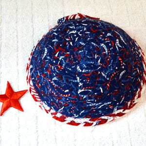 May include: A round, quilted bowl with a patriotic theme. The bowl features a blue fabric with red and white accents, and a red star. The rim is trimmed with red and white striped fabric.