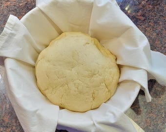May include: A white cloth-lined bowl with a large, round, pale yellow dough ball inside.