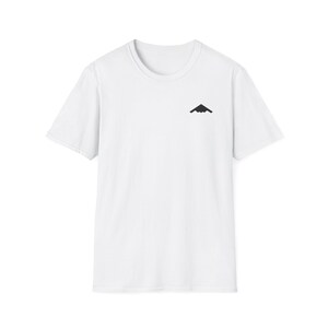 May include: White t-shirt featuring a small black stealth bomber graphic on the upper left chest. The tee has a crew neck and short sleeves. The material appears to be a soft cotton blend.
