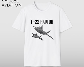 Puede incluir: Camiseta blanca con un gráfico de dos aviones de combate F-22 Raptor grises. El texto "F-22 RAPTOR" está impreso encima de los aviones. La camiseta también tiene el logotipo "Pixel Aviation" en la esquina superior izquierda.