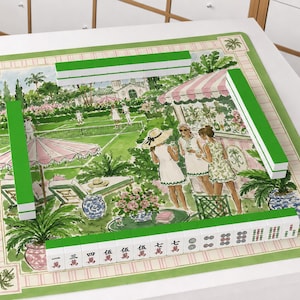 May include: A square mahjong mat featuring a watercolor illustration of a tennis court scene with people, palm trees, and a striped awning. The mat is bordered in green and includes four sets of green and white mahjong tiles arranged on the edges.