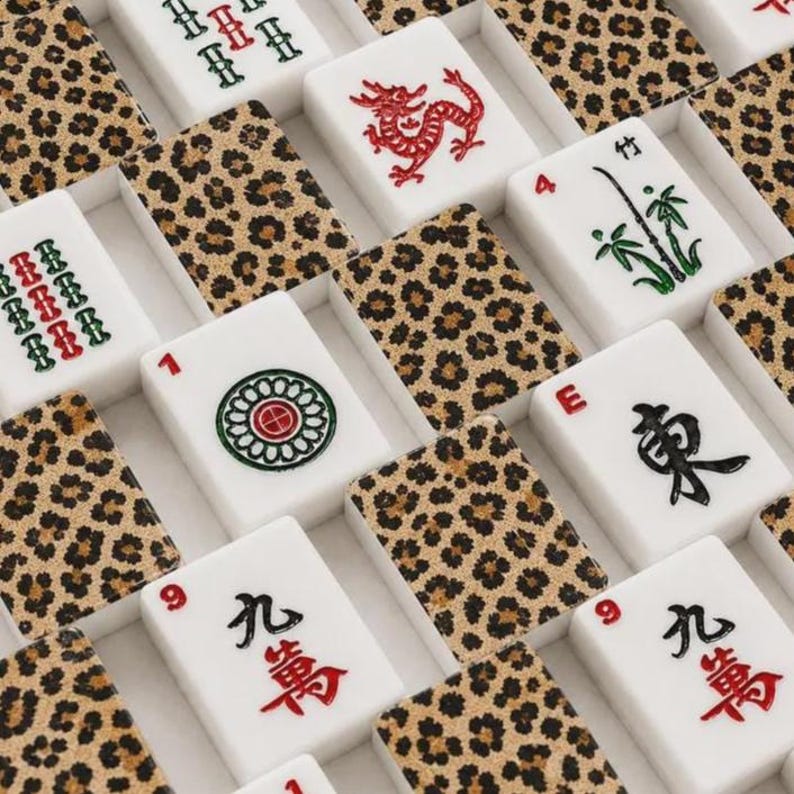 May include: A collection of rectangular mahjong tiles arranged in a grid pattern. The tiles feature either a brown and black leopard print pattern on the back or white faces with various red, green, and black engraved symbols, characters, and numbers.