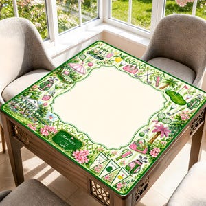 May include: A square table cover featuring a cream-colored center and a decorative border with green stripes, pink flowers, and golf-themed illustrations including golf bags, clubs, carts, and pennants with the text Masters printed on them.