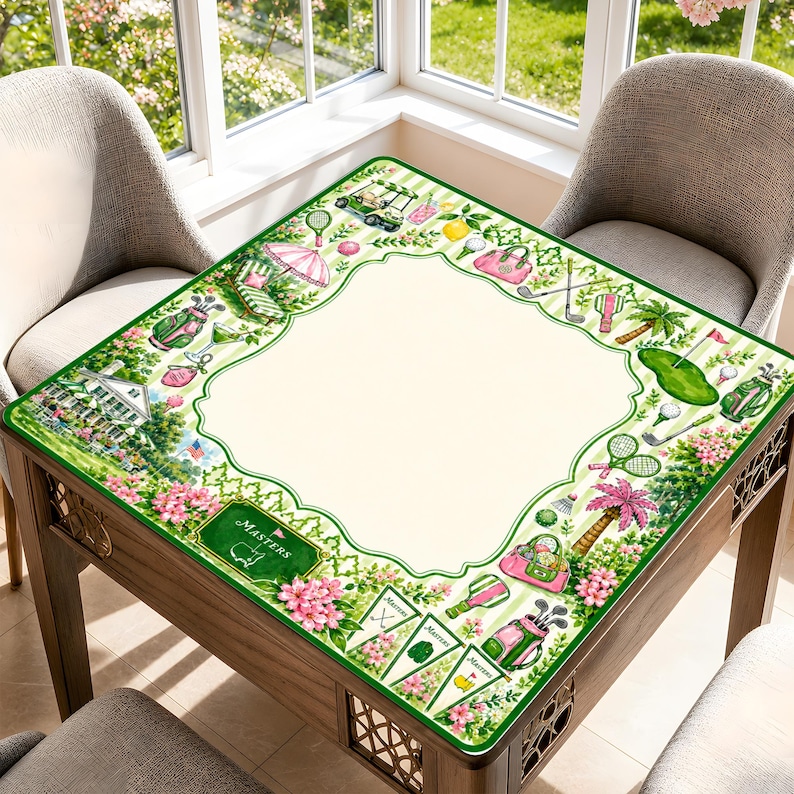 May include: A square table cover featuring a cream-colored center and a decorative border with green stripes, pink flowers, and golf-themed illustrations including golf bags, clubs, carts, and pennants with the text Masters printed on them.