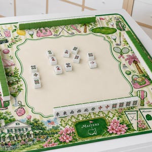 May include: A square mahjong mat featuring a cream-colored center and a green border decorated with golf-themed illustrations, including a clubhouse, golf bags, and clubs. The mat includes green tile racks and white mahjong tiles with symbols.