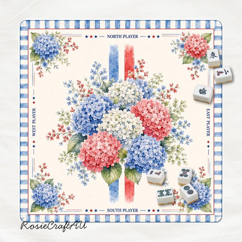 Puede incluir: Un tapete de mahjong cuadrado con un ramo central de hortensias azules, rosas y blancas en acuarela. El borde tiene rayas azules y blancas con etiquetas para los jugadores Norte, Sur, Este y Oeste. Varias fichas de mahjong blancas est&aacute;n dispersas.