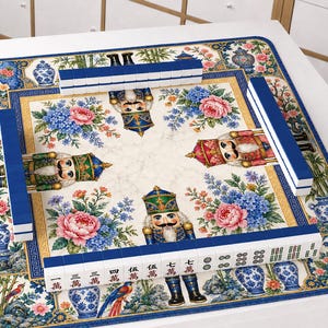 May include: A square mahjong mat featuring a cream-colored center with four nutcracker figures and floral arrangements. The border displays blue and white porcelain vases, birds, and flowers. Four rows of blue and white mahjong tiles are arranged.