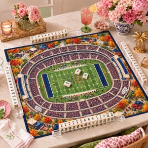 May include: A square mahjong game board featuring a detailed illustration of a football stadium filled with spectators, surrounded by autumn trees. The board includes acrylic tile racks holding white mahjong tiles with black and green characters.