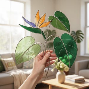 Può includere: Fiore di uccello del paradiso in vetro colorato con tonalità arancioni, viola e verdi. Il design presenta grandi foglie verdi. Il pezzo è sostenuto da sottili steli metallici, creando un accento floreale decorativo.