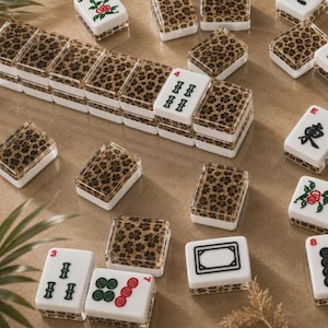 May include: A set of rectangular mahjong tiles featuring a white base with a leopard print pattern on the back. Some tiles display black Chinese characters, green and red floral motifs, or geometric symbols, while others show the leopard print design.