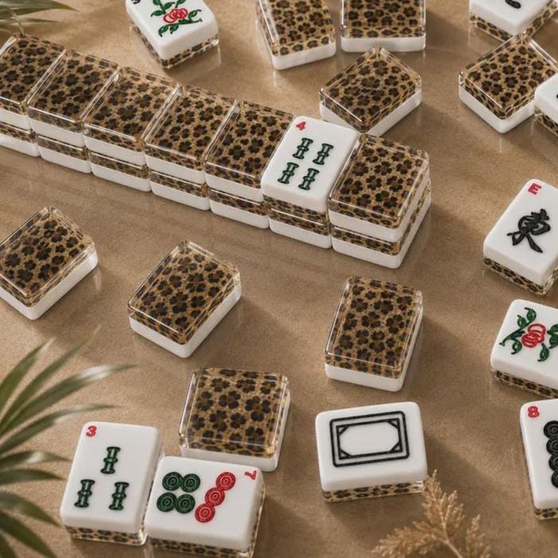 May include: A set of rectangular mahjong tiles featuring a white base with a leopard print pattern on the back. Some tiles display black Chinese characters, green and red floral motifs, or geometric symbols, while others show the leopard print design.
