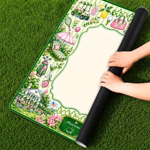 May include: A rectangular mat featuring a white center panel surrounded by a green and white striped border decorated with illustrations of a golf cart, lemon, pink handbag, golf bag, lounge chair, and a clubhouse with the text MASTERS.