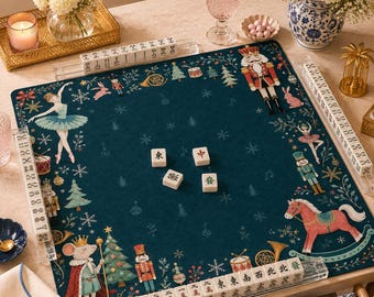 May include: A square dark green mahjong mat featuring a festive Nutcracker-themed print with ballerinas, toy soldiers, a mouse king, and horses. The mat includes four clear acrylic tile racks holding white mahjong tiles with black characters.