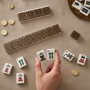 May include: A set of mahjong tiles featuring a brown and black leopard print pattern on the back and traditional Chinese characters or symbols in green and red on the front, accompanied by several small, round, gold-colored metal tokens.