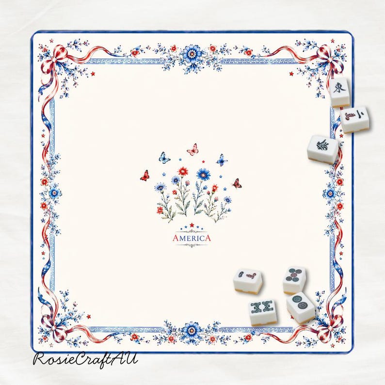 Puede incluir: Un tapete de mahjong cuadrado de color blanco roto con un borde de cintas, flores y mariposas rojas, blancas y azules. El centro muestra un arreglo floral con mariposas y la palabra AMERICA. Cinco fichas de mahjong est&aacute;n esparcidas.