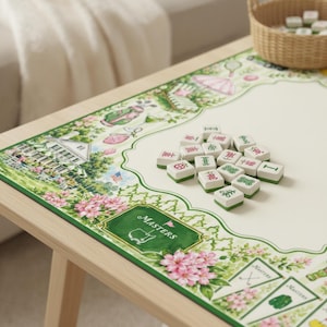 May include: A rectangular game mat featuring a cream-colored center and a decorative border with illustrations of a clubhouse, golf bags, and pink flowers. The word MASTERS is printed on a green rectangular emblem. A pile of white mahjong tiles sits on top.