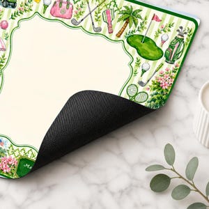 May include: A rectangular desk mat with a cream-colored center and a green and white striped border featuring watercolor illustrations of golf clubs, golf bags, golf balls, palm trees, pink flowers, and a golf green with a flag.
