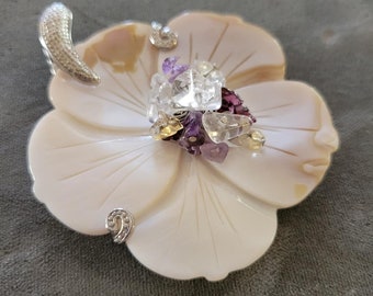 May include: A white shell flower pendant with a silver bail and a cluster of clear, purple, and yellow gemstones in the center.