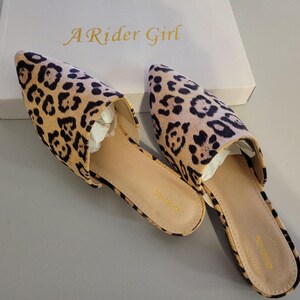 May include: A pair of leopard print slip-on mules with pointed toes. The shoes are tan with black spots and have a light brown sole. The box behind the shoes has the text "A Rider Girl" in gold lettering.