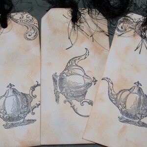 May include: Three vintage-style gift tags with black ribbon and ornate designs. Each tag features a black and white illustration of a teapot with a decorative handle.
