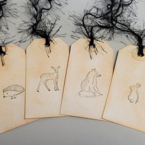 May include: Four brown paper gift tags with black string attached. Each tag features a different animal illustration: a hedgehog, a deer, a fox, and a rabbit.