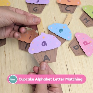Puede incluir: Un conjunto de recortes con forma de cupcake sujetos a pinzas de madera, cada uno con una letra minúscula en el glaseado y una mayúscula en el envoltorio marrón. El texto Cupcake Alphabet Letter Matching es visible en la imagen.