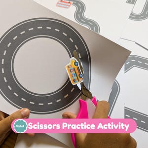 May include: A white sheet of paper featuring a printed gray circular road with white dashed lines. A pair of bright pink scissors is cutting out a small yellow school bus illustration from the paper, which also shows other road shapes.