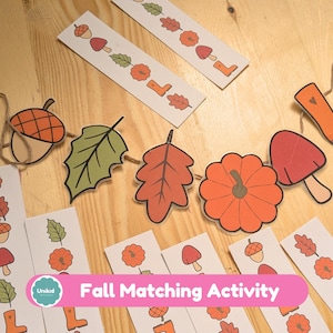 Op de afbeelding: Een herfst-thema matching activiteit met illustraties van eikels, bladeren, pompoenen, paddenstoelen en laarzen. De set bevat bijpassende kaarten en een slinger. De tekst "Fall Matching Activity" is zichtbaar.