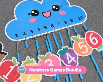 May include: A blue cloud-shaped wall hanging with a smiling face and the numbers 1 through 10 printed in black. Ten jute strings hang from the cloud, each featuring blue plastic beads and colorful fruit-themed number cutouts.
