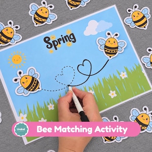 May include: A laminated activity sheet featuring the word Spring, a sun, green grass, and a heart-shaped path. Several bee cutouts are arranged around the sheet, while a marker traces the dotted heart path on the blue background.