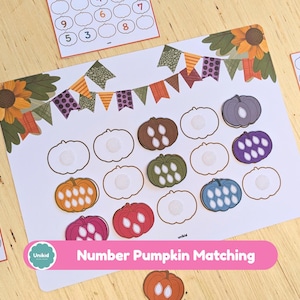May include: A white educational activity sheet featuring a pumpkin-themed number matching game with colourful pumpkin cutouts in orange, red, green, blue, and purple. The sheet includes a decorative bunting banner, sunflowers, and small cards with numbers.