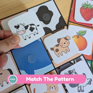 Op de afbeelding: Een kleurrijk kinderspel met illustraties van dieren en fruit. Het spel bevat vierkante kaarten met afbeeldingen van een koe, hond, sinaasappel en aardbei. De tekst "Match The Pattern" staat op een roze banner.