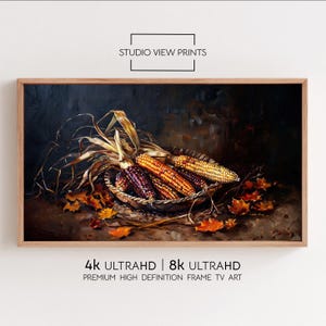 Puede incluir: Una obra de arte enmarcada que presenta una naturaleza muerta de mazorcas de maíz coloridas en una cesta tejida, rodeadas de hojas secas. La obra de arte está en un marco de madera. El texto "STUDIO VIEW PRINTS" y "4K ULTRAHD | 8K ULTRAHD" son visibles.