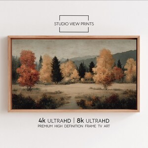 Peut inclure: Une impression encadrée d'un paysage automnal. L'œuvre présente des arbres aux feuilles orange et jaunes vives, sur fond de collines et de ciel voilé. Le cadre est de couleur marron clair. Le texte "STUDIO VIEW PRINTS" est visible.