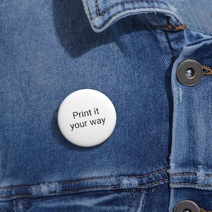 May include: A white button with the text "Print it your way" in black, set against a blue denim jacket. The button is round and appears to be a pinback button, commonly used for personal expression or promotional purposes.