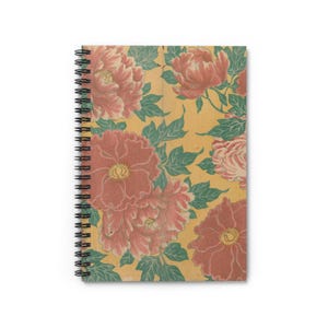 以下が含まれることがあります： 花柄のノート。表紙には、黄色の背景に、大きなピンク色の牡丹と黄色の中心、緑の葉が描かれています。ノートは黒いスパイラルバインディングです。