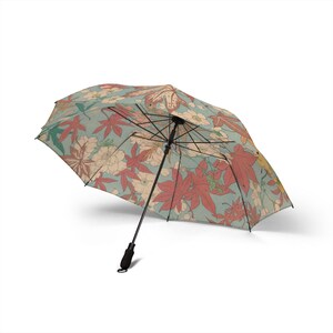 May include: An open umbrella with a black handle and frame. The canopy displays a floral pattern with red, cream, and green leaves and flowers on a light blue backdrop. The umbrella is angled slightly to the left.