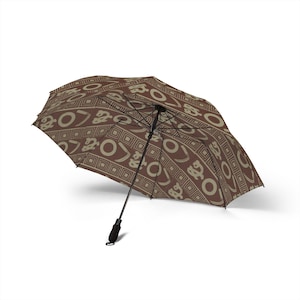 May include: Brown and beige patterned umbrella. The umbrella has a repeating geometric design with circular and angular shapes. The handle is black, and the umbrella is open, displaying its full design.