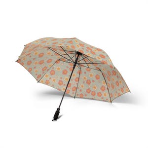 May include: An open umbrella with a floral pattern. The umbrella's canopy is light green with a repeating design of orange and pink flowers. It has a black handle and frame, and is set against a white background.