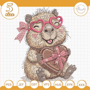 Puede incluir: Diseño bordado de un capibara sonriente con gafas rosas en forma de corazón y sosteniendo una caja de regalo en forma de corazón con un lazo rosa. El diseño incluye el texto "5 size" y varias etiquetas de formato de archivo.