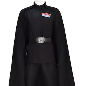 May include: A black costume with a high collar, cape, and belt. The outfit includes a jacket, trousers, and a belt with a silver buckle. A small patch with red, white, and blue rectangles is on the chest. The costume is displayed on a mannequin.