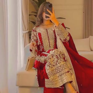 May include: A red velvet ensemble with gold embroidery. The outfit includes a long-sleeved top and matching pants. A gold clutch and gold heels complete the look. The outfit is suitable for special occasions.