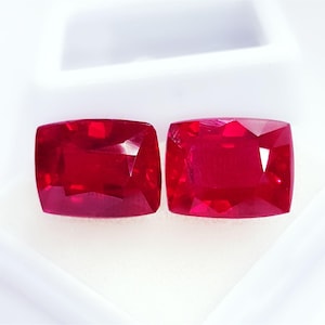 Peut inclure: Deux pierres précieuses rouge vif et profond avec une taille coussin et des surfaces facettées. Ces pierres libres présentent un haut niveau de clarté et de transparence, reflétant la lumière sur leurs surfaces polies. Elles sont rectangulaires.