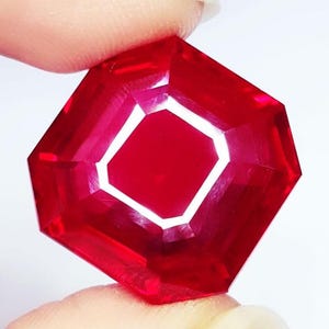 Peut inclure: Une pierre précieuse rouge vif et profonde avec une taille à facettes octogonale. La pierre présente une grande clarté et un éclat brillant, avec des bords géométriques nets reflétant la lumière sur sa surface polie, révélant une teinte cramoisie riche.